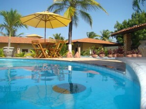 Ein Pool mit klarem, blauem Wasser, umgeben von Palmen und einem Gebäude mit einem Ziegeldach.