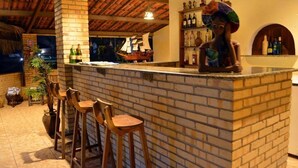 A bar area with a brick counter, wooden stools, and a ship model. - Pousada Oceania (São Gonçalo do Amarante)