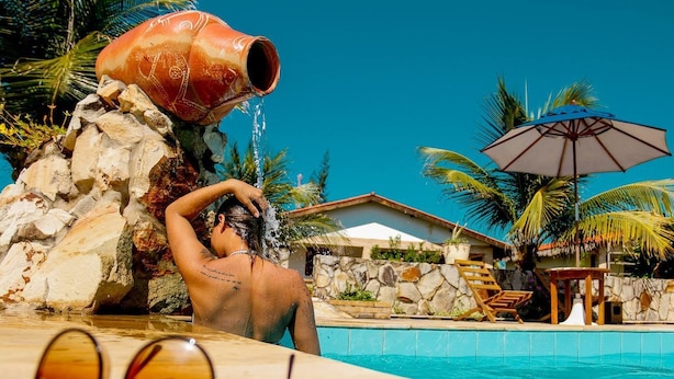 A pool area with a water feature, lounge chairs, and a stone wall. - Pousada Oceania (São Gonçalo do Amarante)