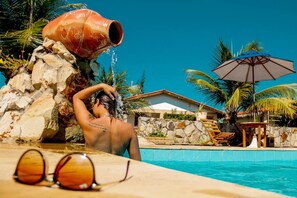 A pool area with a water feature, lounge chairs, and a stone wall. - Pousada Oceania (São Gonçalo do Amarante)
