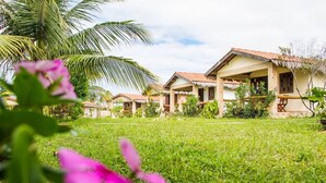 A row of traditional-style houses with tiled roofs, surrounded by lush greenery and palm trees. - Pousada Oceania (São Gonçalo do Amarante)