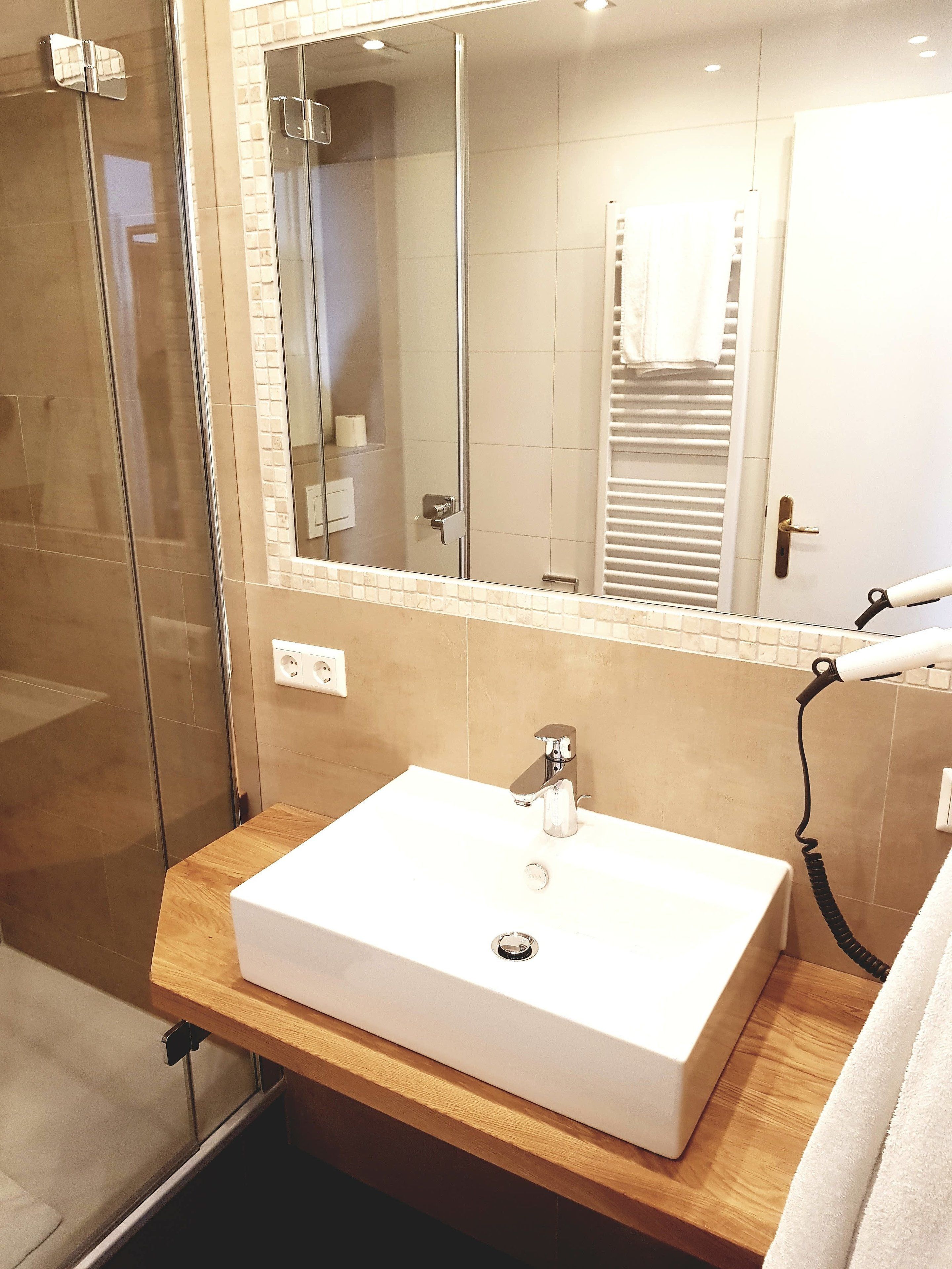 A bathroom with a white sink, a glass shower enclosure, and a mirror with a towel hanging on the door.