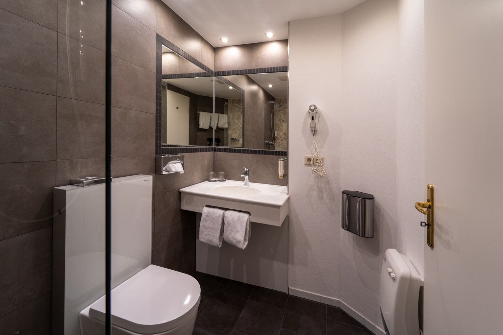 Un baño moderno con ducha de vidrio, inodoro blanco, lavamanos con espejo y un perchero para toallas.