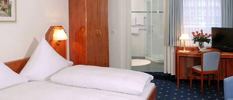 Habitación de hotel con cama, escritorio con silla, televisión, armario y baño visible a través de una puerta abierta.