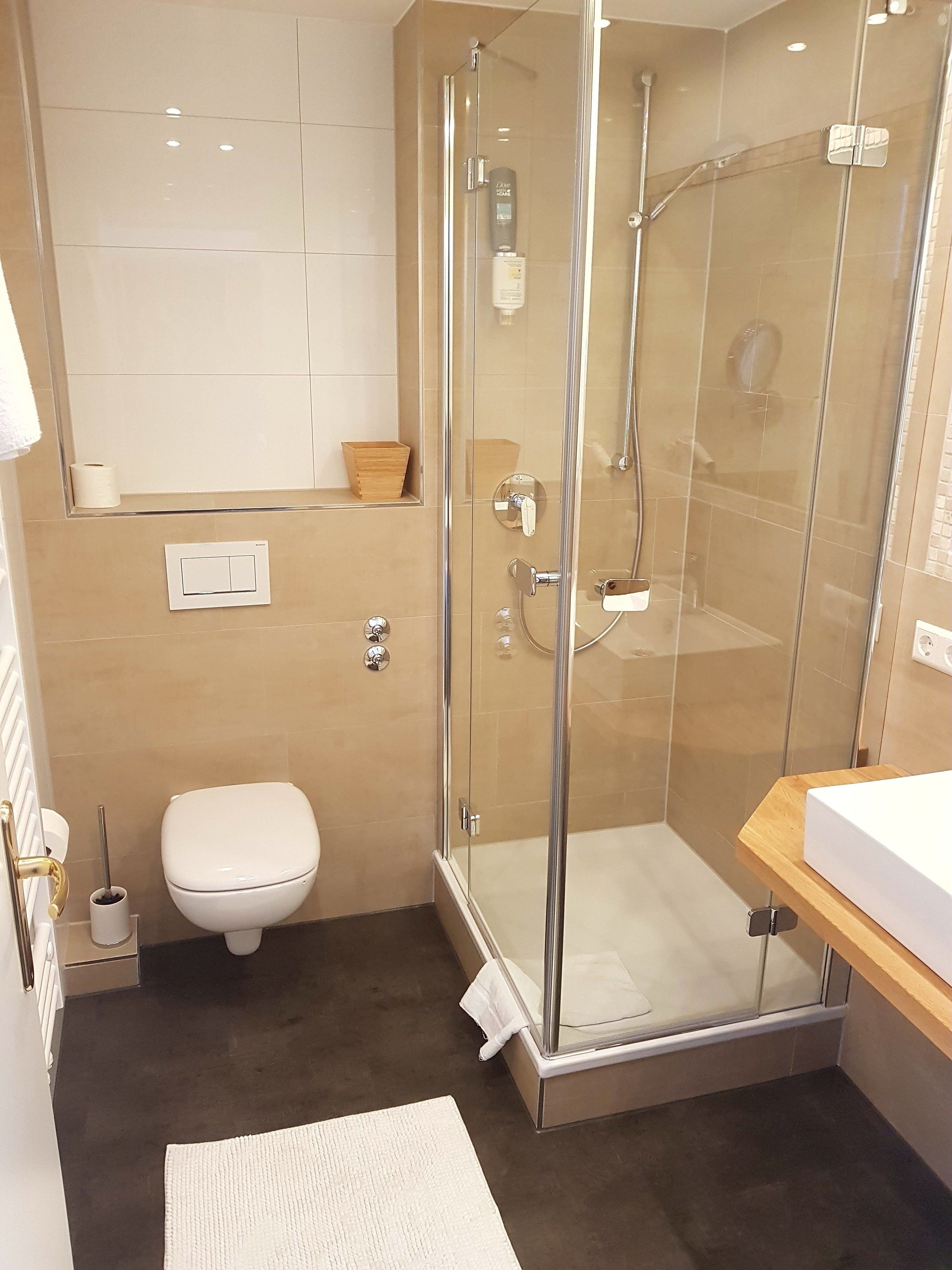 Un baño moderno con ducha envuelta en vidrio, inodoro y lavabo con encimera de madera.