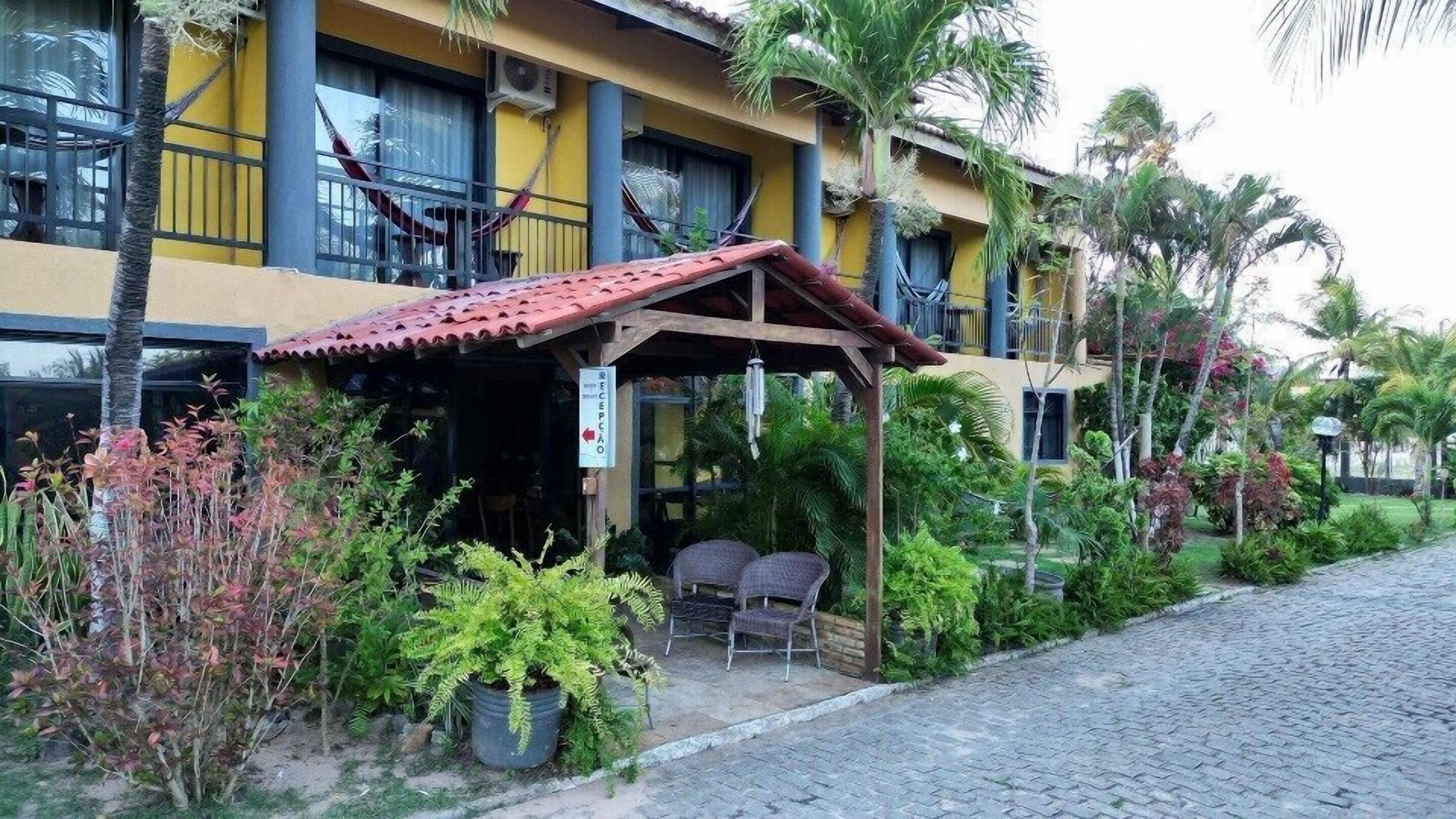 Un hotel con un área de estar al aire libre techada, un sendero pavimentado y abundante vegetación.