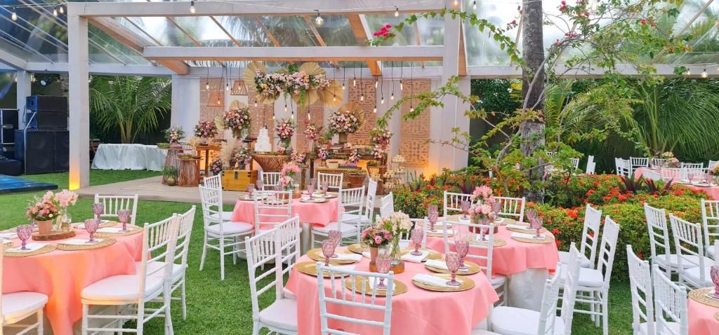 An outdoor event space with round tables, white chairs, and pink tablecloths.