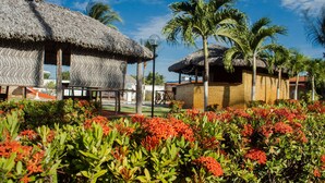 A resort with thatched-roof structures, palm trees, and vibrant red flowers. - Pousada Brasil Cumbuco (Caucaia)