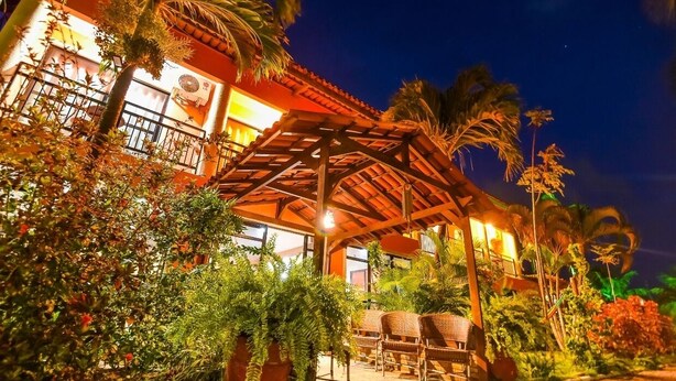 A building with a covered patio area, surrounded by lush greenery and palm trees. - Pousada Brasil Cumbuco (Caucaia)