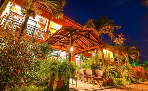 A building with a covered patio area, surrounded by lush greenery and palm trees. - Pousada Brasil Cumbuco (Caucaia)