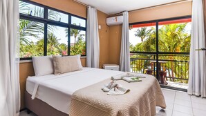 A hotel room with a large bed, a balcony with a view of palm trees, and an air conditioning unit. - Pousada Brasil Cumbuco (Caucaia)