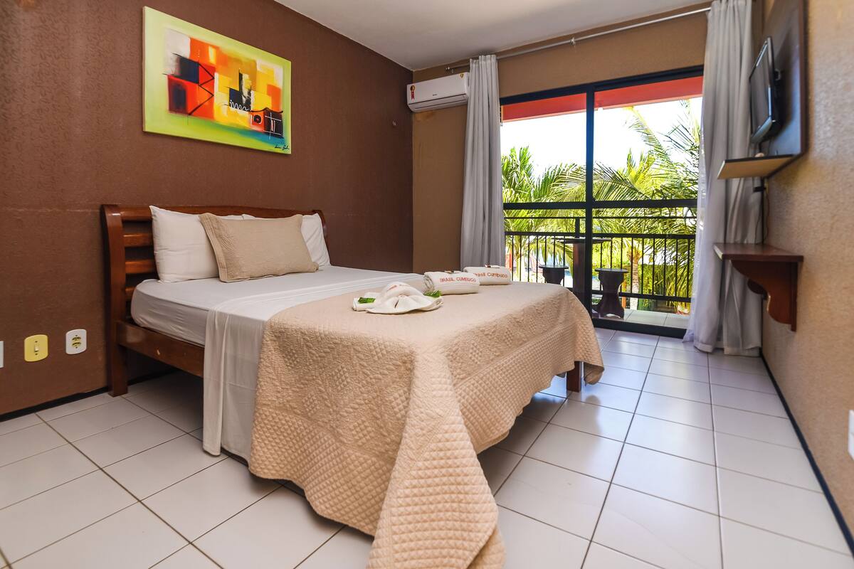 A hotel room with a bed, a balcony with a view, and a painting on the wall.