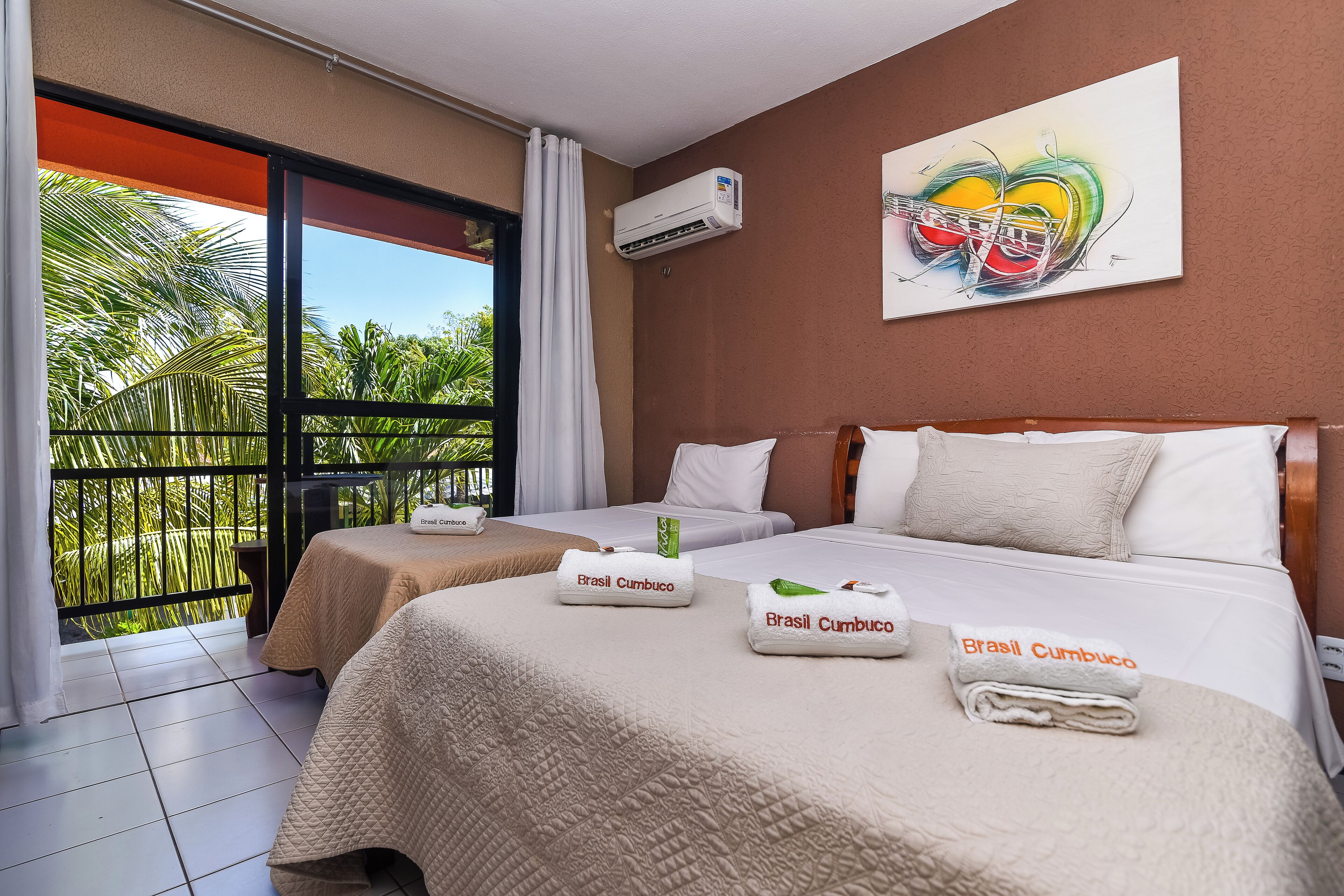 A hotel room with two beds, a balcony with a view of palm trees, and a painting on the wall.