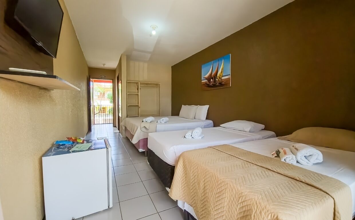 A hotel room with three beds, a TV, and a desk with a refrigerator.