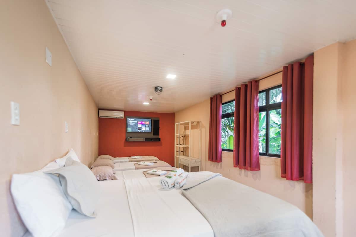 A hotel room with three beds, a TV, a wardrobe, and a window with curtains.