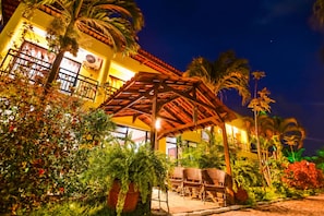 A hotel with a covered outdoor seating area, palm trees, and a yellow facade at night. - Pousada Brasil Cumbuco (Caucaia)
