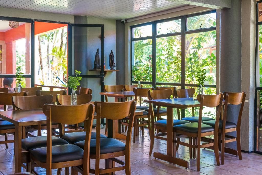 Un restaurante con mesas y sillas de madera, ventanas amplias con vistas a la vegetación y suelo de baldosas.