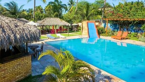 A swimming pool with lounge chairs, a slide, and palm trees. - Pousada Brasil Cumbuco (Caucaia)