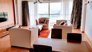 A modern living room with a flat-screen TV mounted on the wall, a sofa, two armchairs, a coffee table, and a wooden floor. - Lymack Suites (Nairobi)