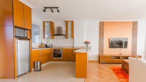 A modern kitchen with wooden cabinets, a stainless steel refrigerator, and a built-in oven. There is a small trash bin and a wooden island with a vase of flowers. - Lymack Suites (Nairobi)