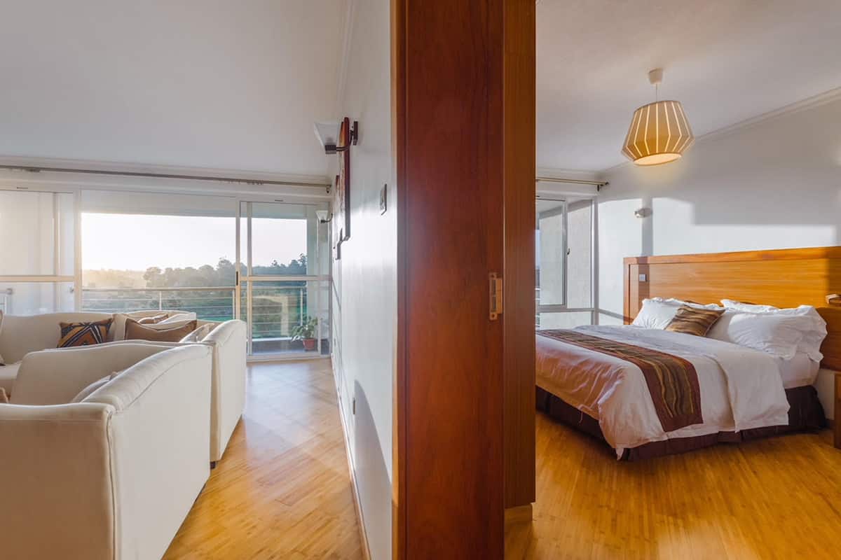A modern bedroom with a wooden headboard, a large bed, and a view of the outdoors through a sliding glass door.