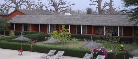 A hotel with a poolside area, lounge chairs, and a well-maintained garden with hedges and trees.