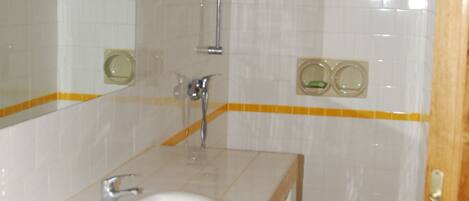 Un baño con lavamanos blanco, espejo y paredes con azulejos.