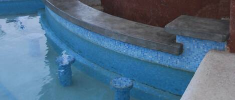 A pool area with steps leading into the water, a covered seating area, and a thatched roof structure.