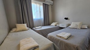 Habitación de hotel con dos camas individuales, una mesita de noche pequeña, aire acondicionado instalado en la pared y una ventana con cortinas.
