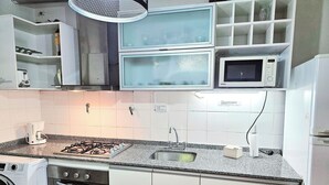 Cocina compacta equipada con estufa a gas, microondas, horno empotrado, pileta y lavadora.