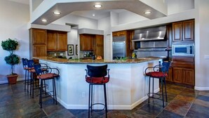 A spacious kitchen with a central island, wooden cabinets, stainless steel appliances, and a potted plant. - Vista Bonita (Scottsdale)