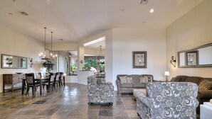 A spacious living room with a dining area, featuring a large chandelier, patterned sofas, and a view into the kitchen. - Vista Bonita (Scottsdale)