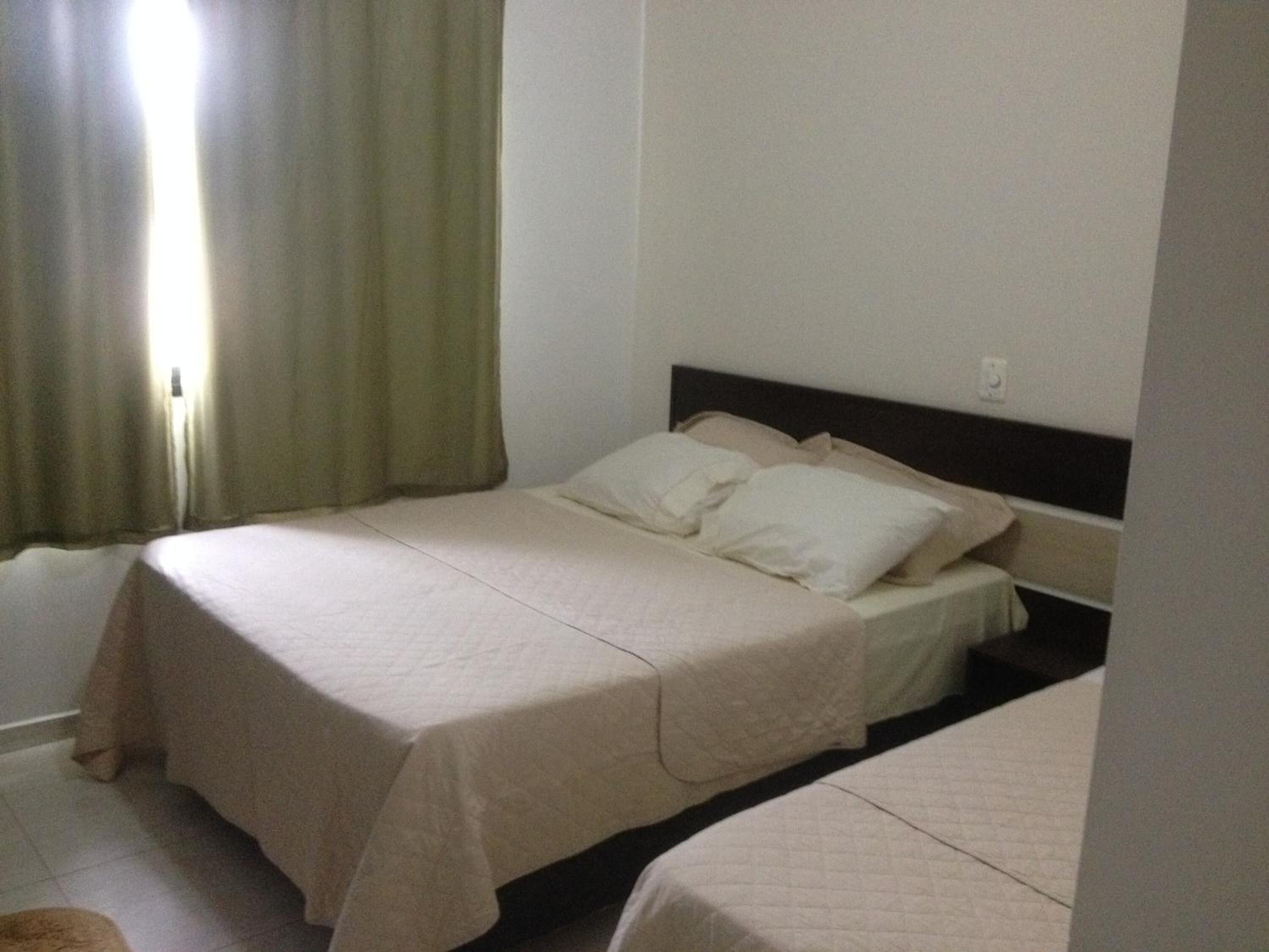 A single bed with a headboard, a window with curtains, and a tiled floor.