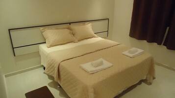 Una cama bien hecha con cabecera, dos almohadas y dos toallas dobladas al pie.