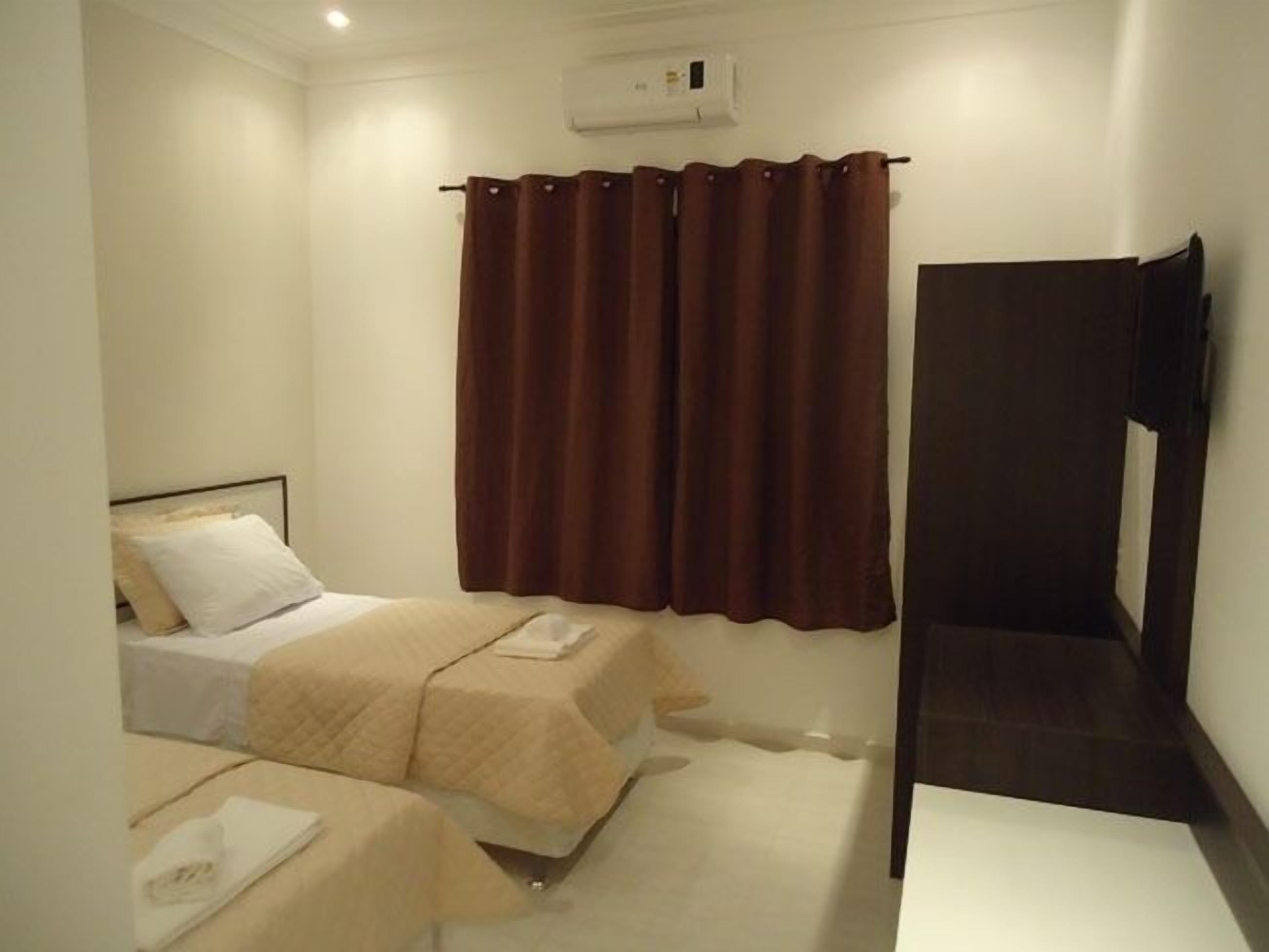 Quarto de hotel com duas camas, televisão de tela plana e unidade de ar condicionado na parede.