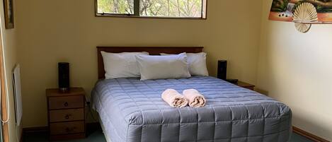 A bedroom with a large bed, a nightstand, a dresser, a window, and a wall decoration.