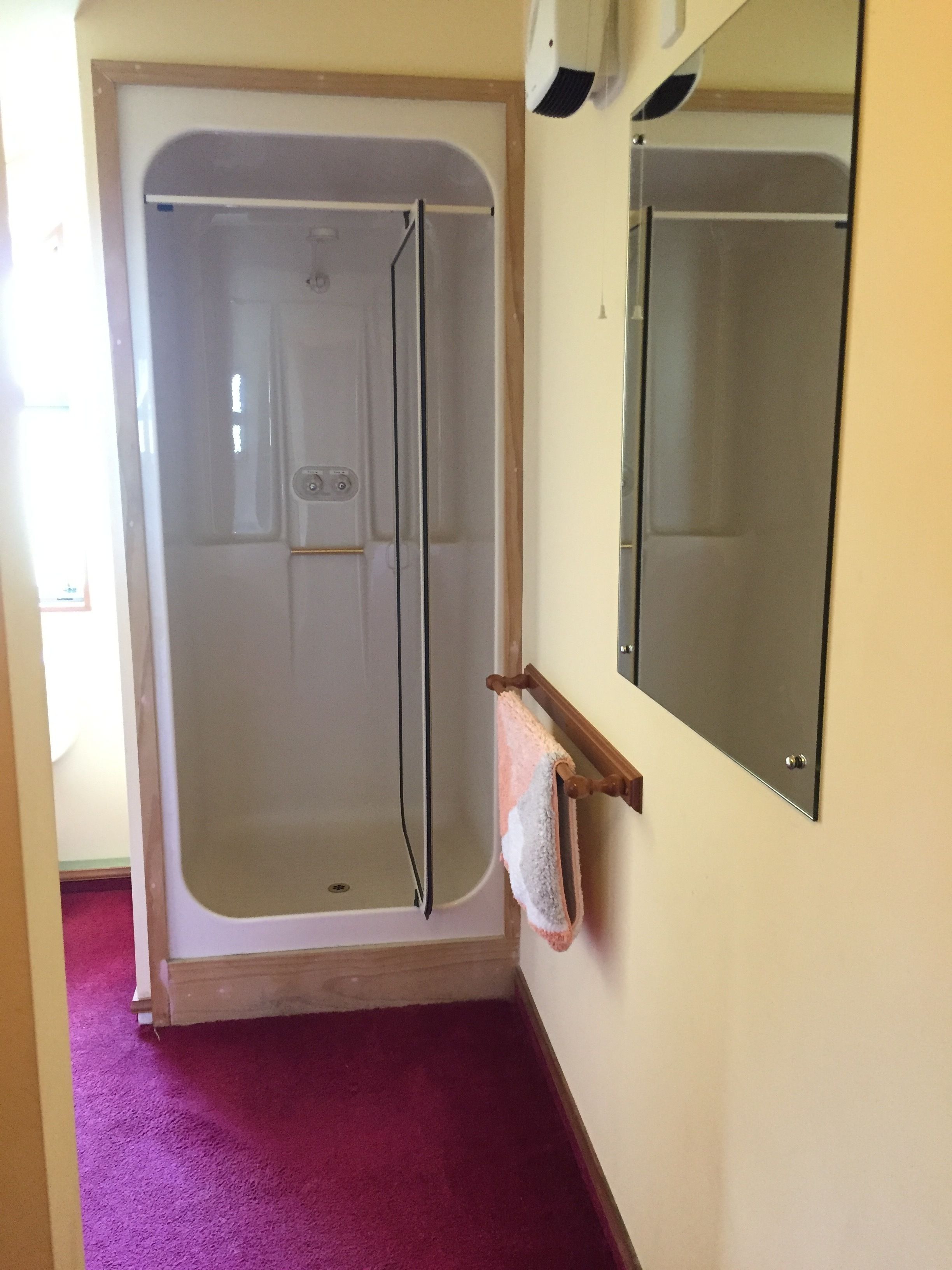 Une douche à l’italienne avec une porte en verre, un porte-serviettes en bois et un sol recouvert d’une moquette violette.