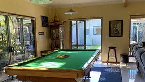 Une table de billard dans une pièce bien éclairée, dotée de grandes fenêtres, d’une armoire et d’un tableau encadré au mur.