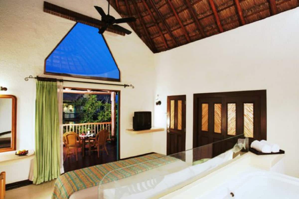Ein Schlafzimmer mit Bett, Deckenventilator, Fernseher und Blick ins Freie.