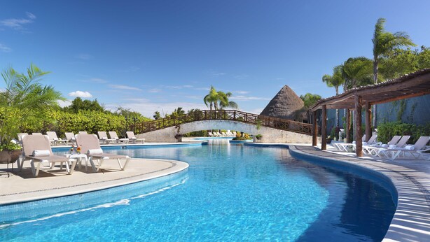 A swimming pool with lounge chairs and a stone bridge. - Bel Air Collection Resort & Spa Riviera Maya - All Inclusive (Xpu-Ha)