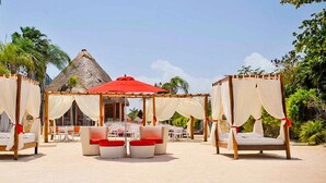 A beachside setting with a thatched-roof structure, a red umbrella, and white canopied beds with red cushions. - Bel Air Collection Resort & Spa Riviera Maya - All Inclusive (Xpu-Ha)