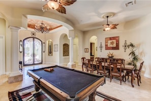 A pool table in a spacious room with a dining area, arched doorways, and ceiling fans. - Hayden Manor (Scottsdale)