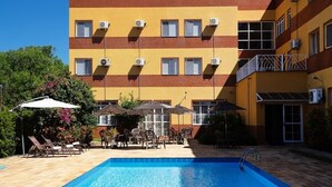 A swimming pool with lounge chairs and umbrellas, a multi-story building with air conditioning units, and a clear blue sky. - Itapetinga Hotel (Atibaia)