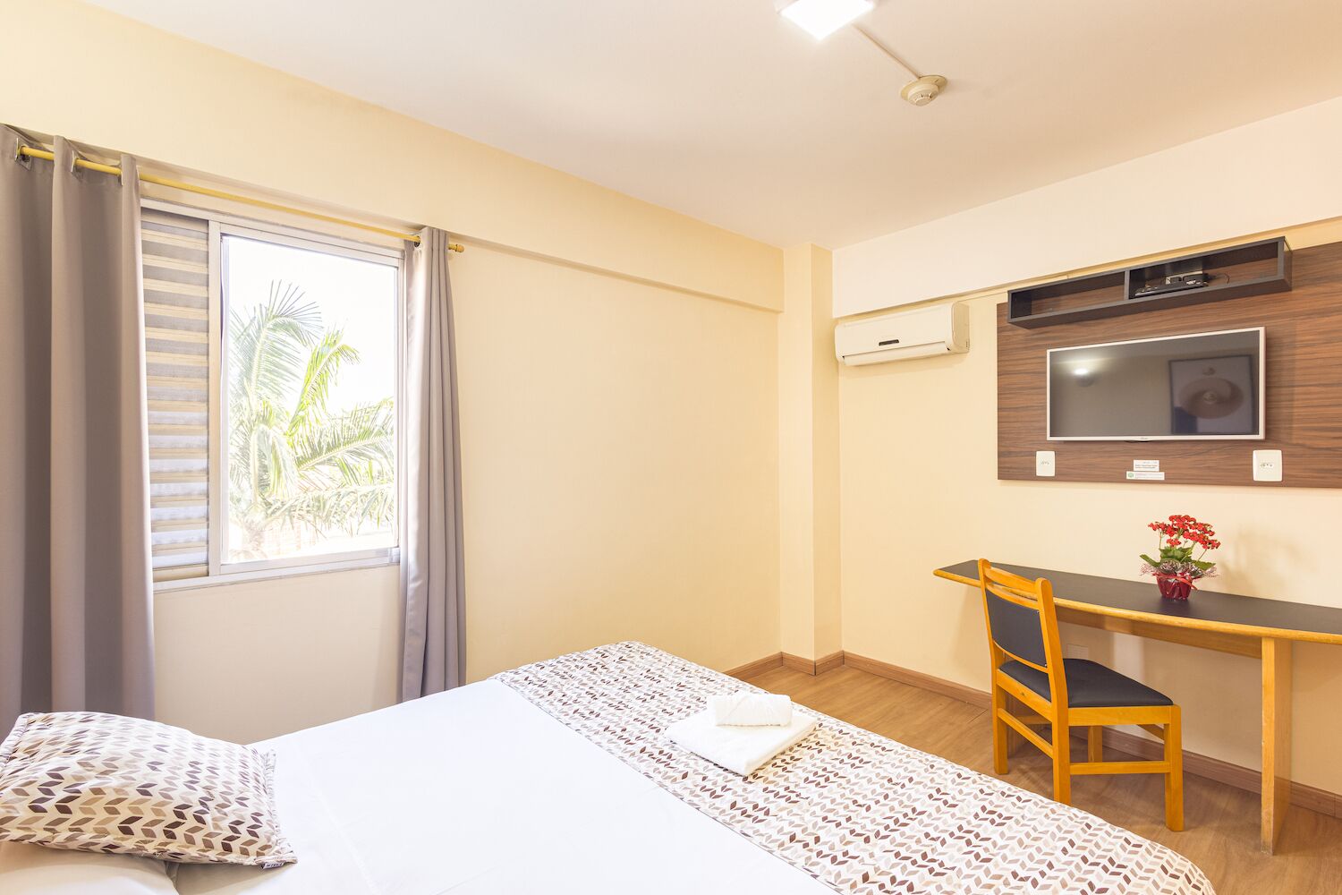 Une chambre d’hôtel équipée d’un lit, d’un bureau, d’une chaise, d’une télévision et d’une fenêtre avec des rideaux.