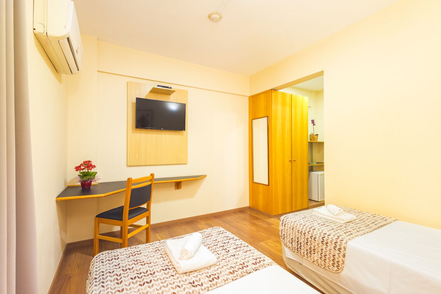 A hotel room with two beds, a desk with a chair, a TV mounted on the wall, and a wardrobe.