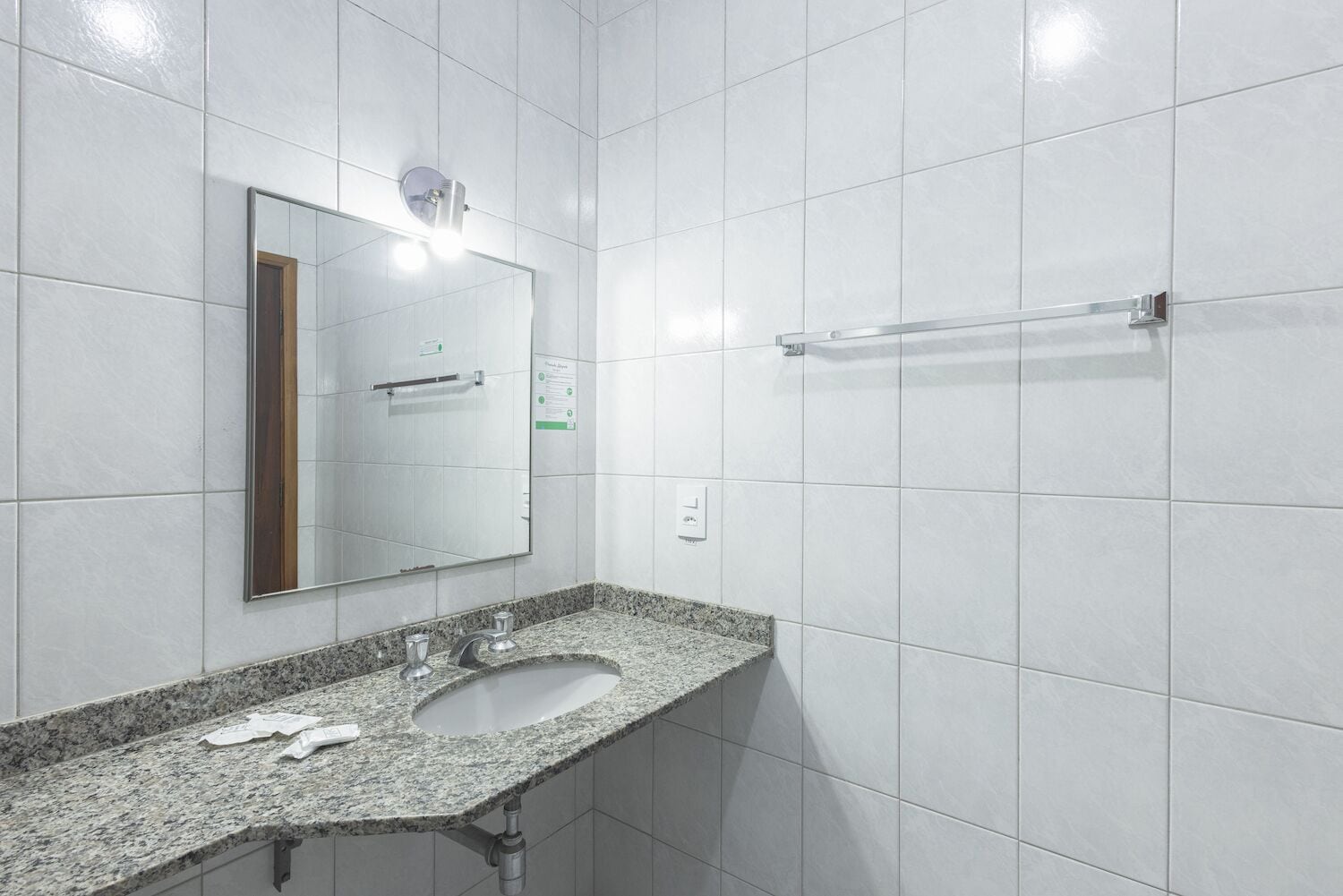A bathroom with white tiles, a granite countertop, a sink, a mirror, and a towel rack.