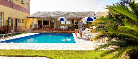 Una piscina con solárium de baldosas, rodeada de césped y palmeras.