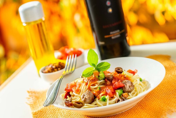 A plate of spaghetti with tomato sauce, meat, and vegetables, accompanied by a fork and a small bowl of sauce. - Itapetinga Hotel (Atibaia)