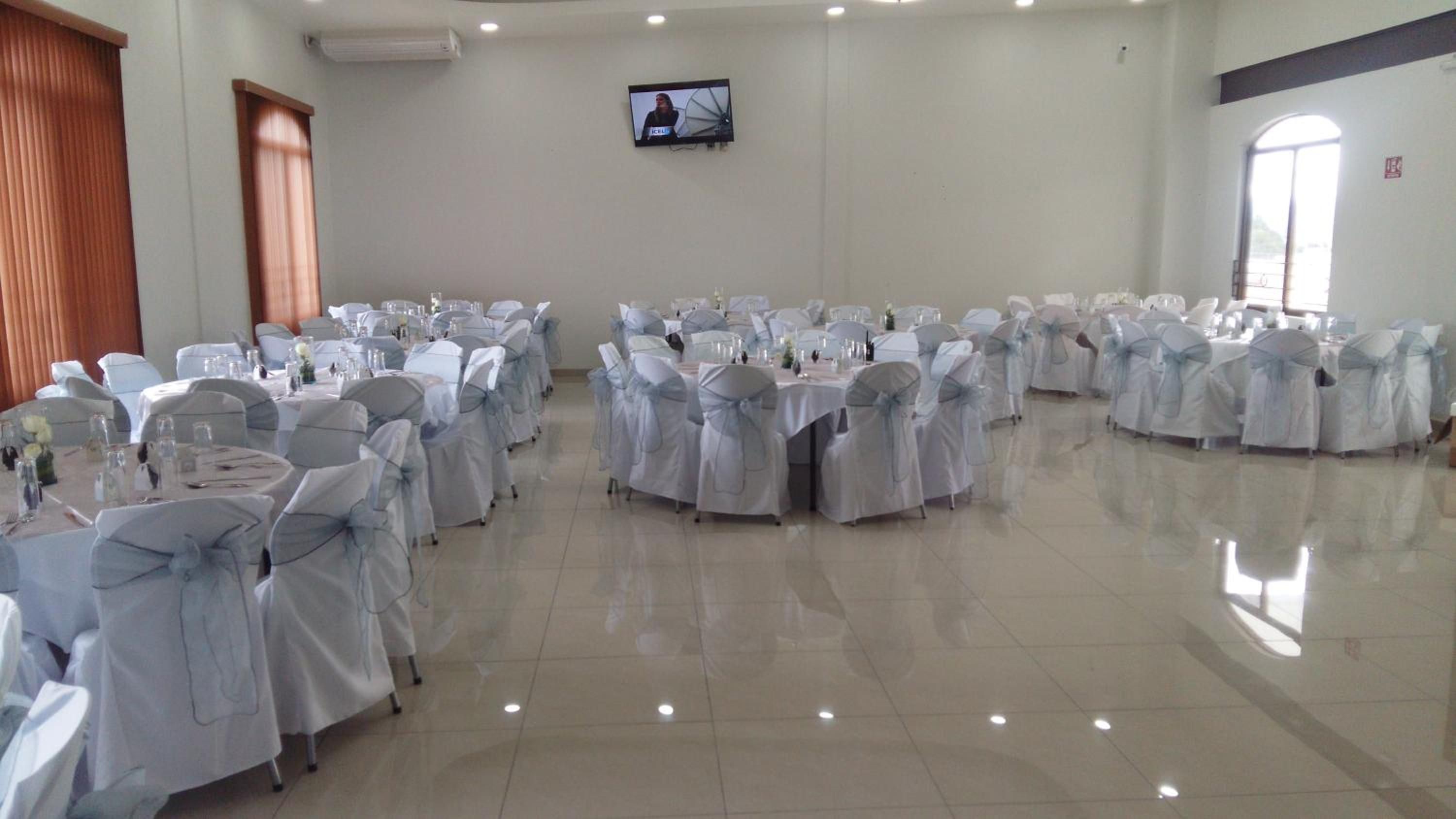 A conference room with multiple tables and chairs, a television mounted on the wall, and a large window.