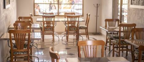 A restaurant with wooden chairs and tables, a large window with a view of the street, and a metal pole in the corner.
